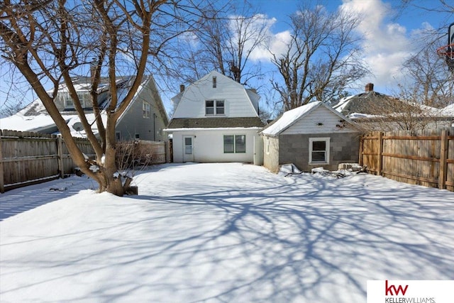 snow covered back of property featuring a fenced backyard and a gambrel roof