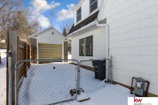 snow covered property featuring a garage, a gate, fence, and an outdoor structure