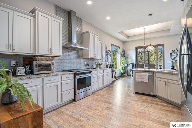 kitchen with decorative light fixtures, a toaster, stainless steel appliances, a raised ceiling, and wall chimney exhaust hood