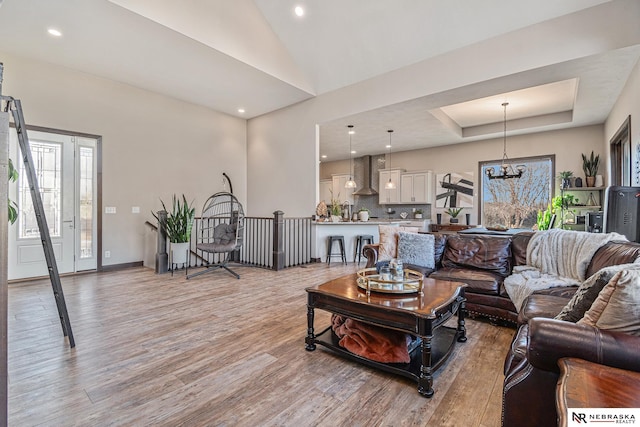 living area with a chandelier, light wood-type flooring, a tray ceiling, and recessed lighting