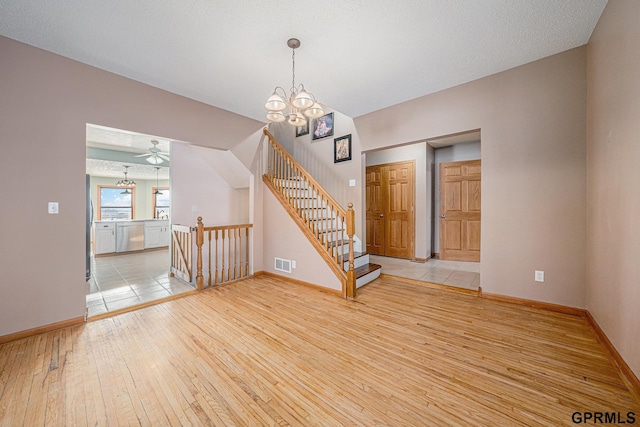 interior space featuring visible vents, stairway, light wood-style floors, baseboards, and ceiling fan with notable chandelier