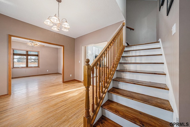 stairs featuring baseboards, a notable chandelier, and wood finished floors