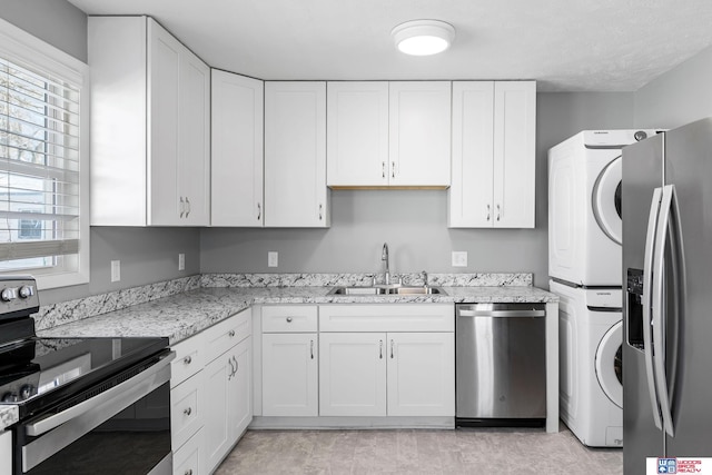 kitchen featuring appliances with stainless steel finishes, stacked washer and dryer, white cabinets, and a sink