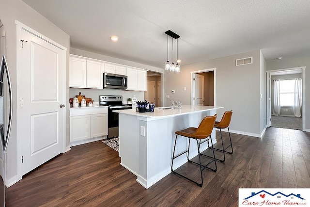 kitchen featuring light countertops, hanging light fixtures, appliances with stainless steel finishes, white cabinets, and a kitchen island with sink