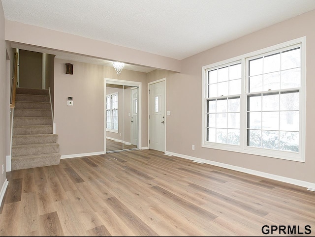 foyer entrance with light wood finished floors, stairs, baseboards, and a textured ceiling