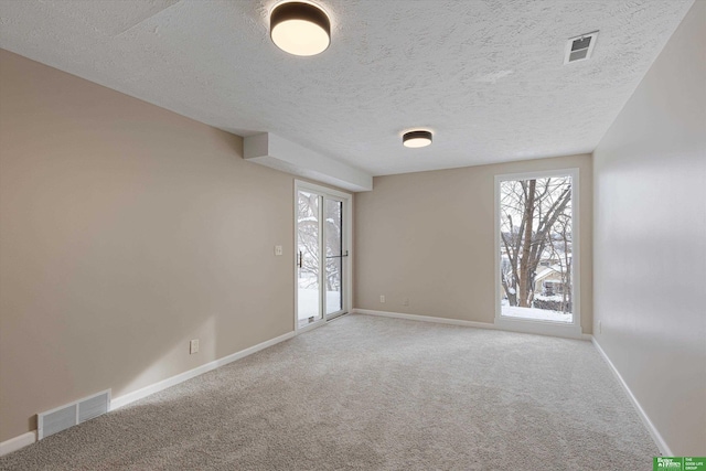 carpeted spare room featuring a textured ceiling, visible vents, and baseboards