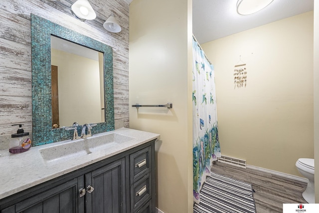 bathroom featuring toilet, wood finished floors, vanity, visible vents, and baseboards