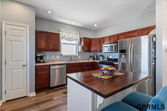 kitchen featuring a sink, wood counters, appliances with stainless steel finishes, a center island, and a kitchen bar