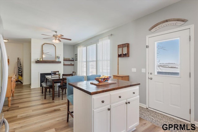 kitchen with light wood-style flooring, a large fireplace, a kitchen island, white cabinetry, and open floor plan