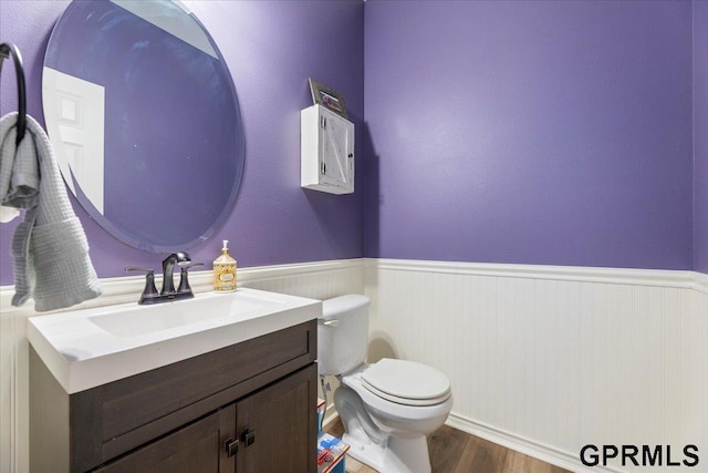 half bathroom featuring wainscoting, vanity, toilet, and wood finished floors