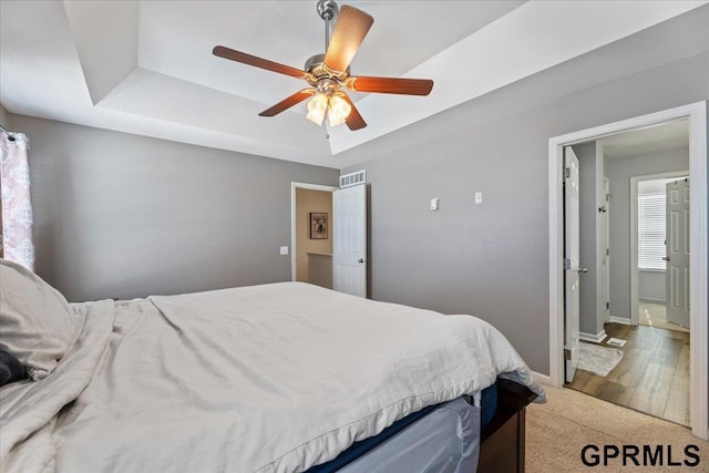 bedroom with wood finished floors, a ceiling fan, visible vents, baseboards, and a tray ceiling