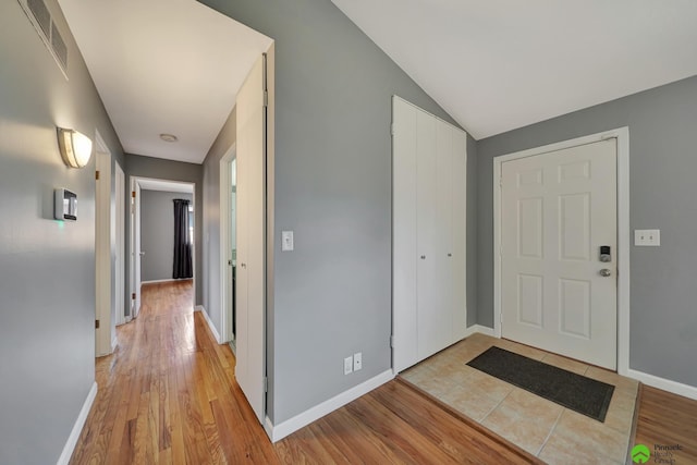 foyer with visible vents, baseboards, lofted ceiling, and light wood-style floors