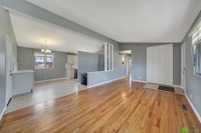 unfurnished living room with visible vents, an inviting chandelier, light wood finished floors, baseboards, and vaulted ceiling