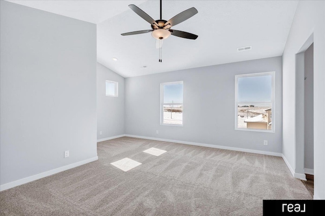 spare room featuring ceiling fan, light colored carpet, visible vents, baseboards, and vaulted ceiling