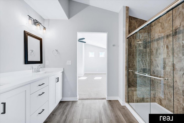 bathroom with double vanity, a stall shower, baseboards, wood finished floors, and a sink