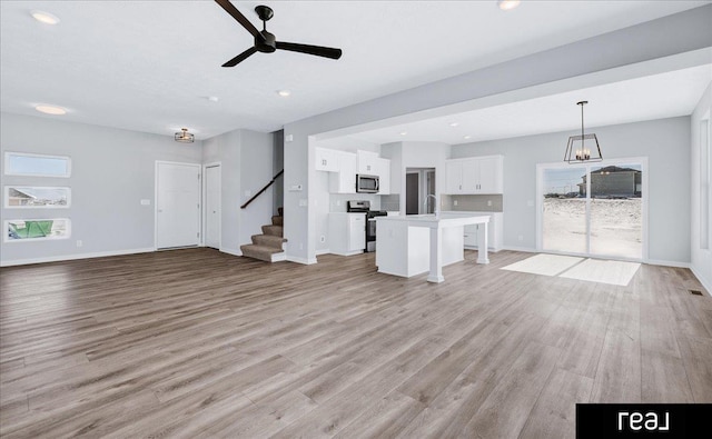 unfurnished living room with light wood-style floors, stairs, and baseboards