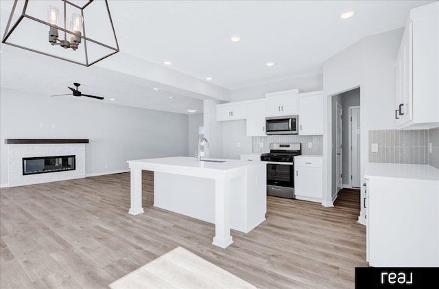 kitchen featuring stainless steel appliances, light countertops, open floor plan, white cabinets, and an island with sink