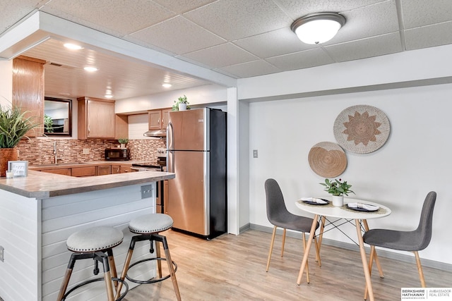 kitchen featuring stainless steel appliances, light countertops, backsplash, a sink, and a kitchen breakfast bar