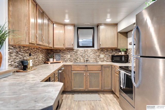 kitchen featuring stainless steel appliances, light wood-style floors, a sink, and decorative backsplash