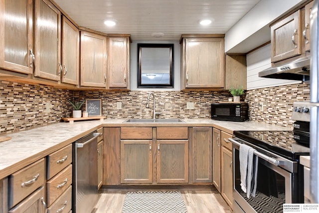 kitchen with stainless steel appliances, a sink, light countertops, backsplash, and light wood finished floors