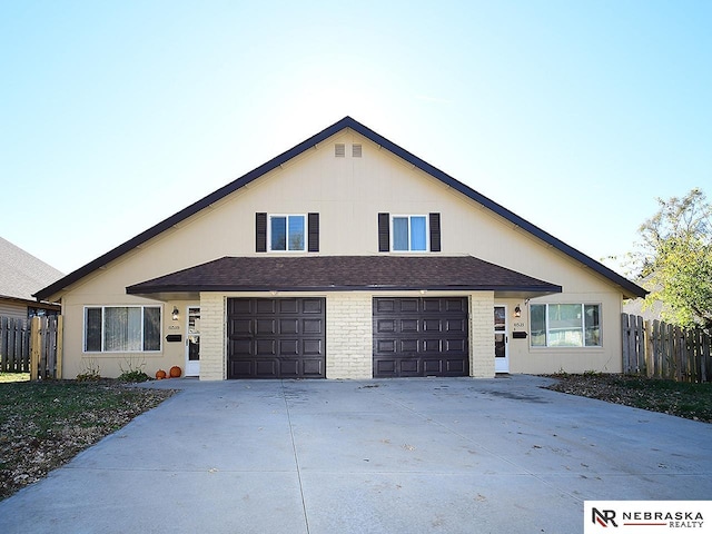 view of front facade featuring driveway, brick siding, an attached garage, and fence