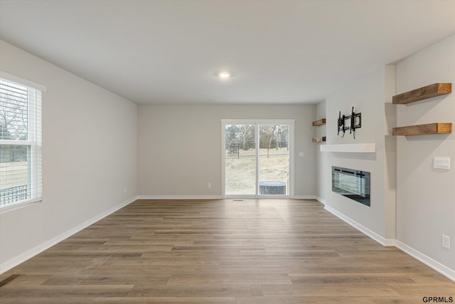 unfurnished living room with light wood-style flooring, baseboards, and a glass covered fireplace