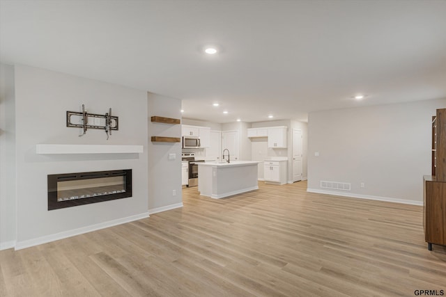 unfurnished living room with light wood-type flooring, recessed lighting, visible vents, and a glass covered fireplace