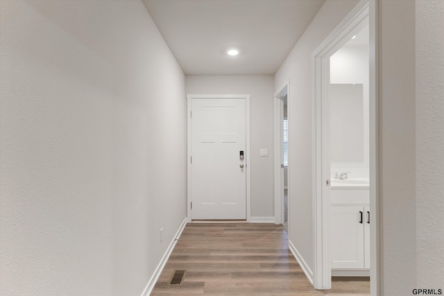 hall with visible vents, a sink, baseboards, and wood finished floors