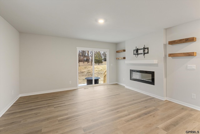 unfurnished living room featuring a glass covered fireplace, baseboards, and wood finished floors