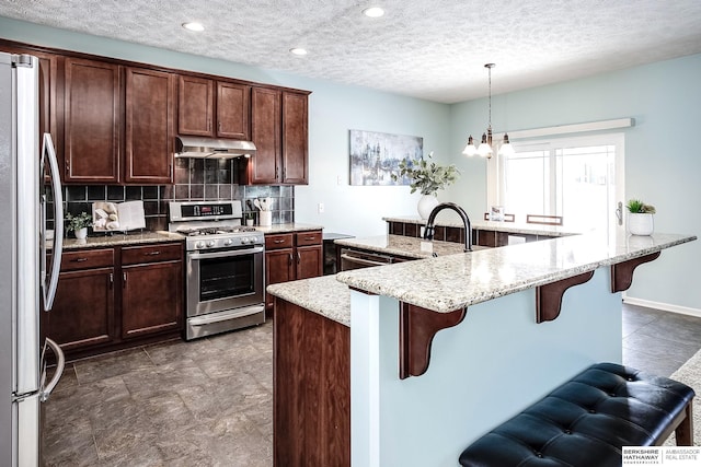 kitchen featuring light stone counters, a breakfast bar area, hanging light fixtures, stainless steel appliances, and under cabinet range hood