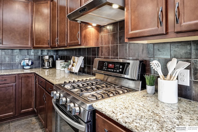 kitchen featuring stainless steel gas range, range hood, backsplash, and light stone countertops