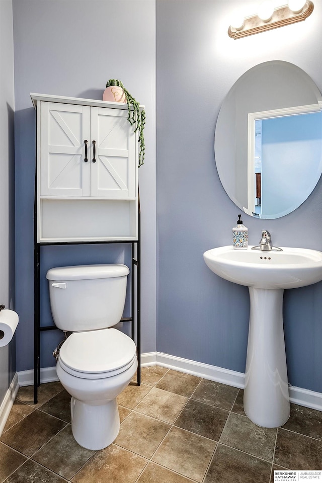 half bathroom featuring toilet, tile patterned flooring, baseboards, and a sink