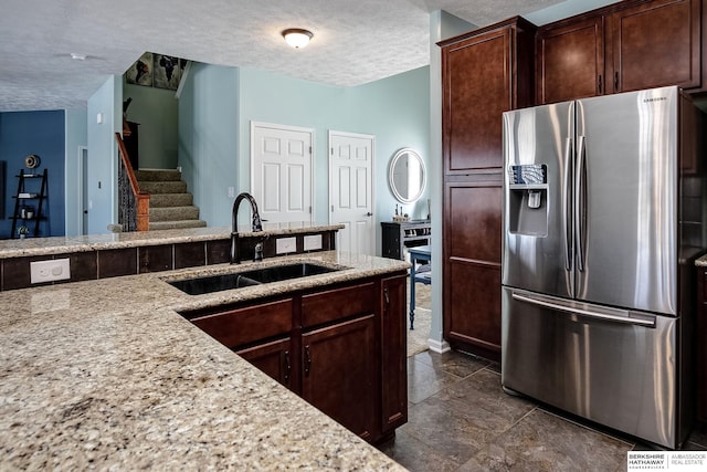 kitchen with a textured ceiling, light stone counters, stainless steel refrigerator with ice dispenser, and a sink