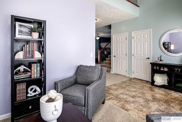 sitting room featuring ceiling fan, a textured ceiling, baseboards, and stairs