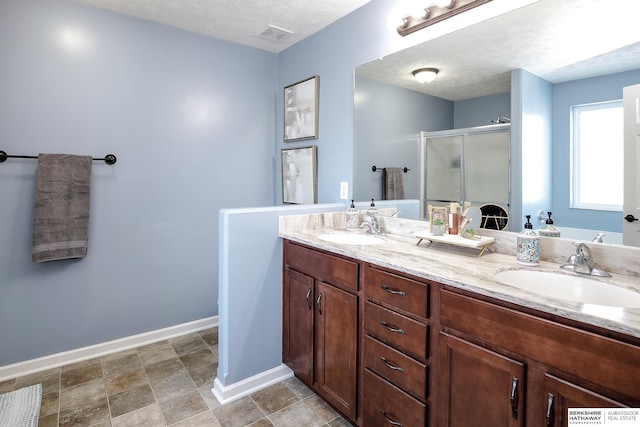 bathroom featuring baseboards, double vanity, a sink, and a shower stall