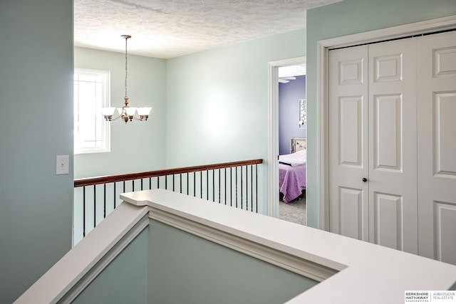 hall featuring a textured ceiling, carpet flooring, an upstairs landing, and an inviting chandelier