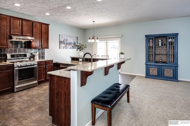 kitchen featuring light stone counters, hanging light fixtures, gas stove, under cabinet range hood, and a kitchen breakfast bar