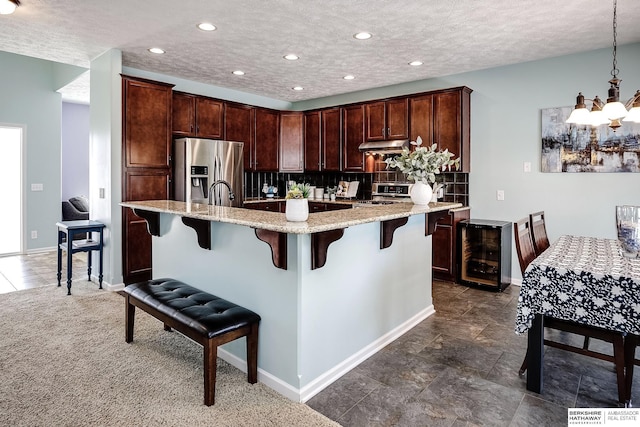 kitchen with stainless steel appliances, pendant lighting, beverage cooler, and a kitchen breakfast bar