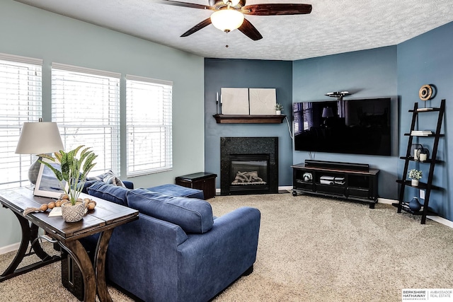 carpeted living room with a ceiling fan, a glass covered fireplace, a textured ceiling, and baseboards