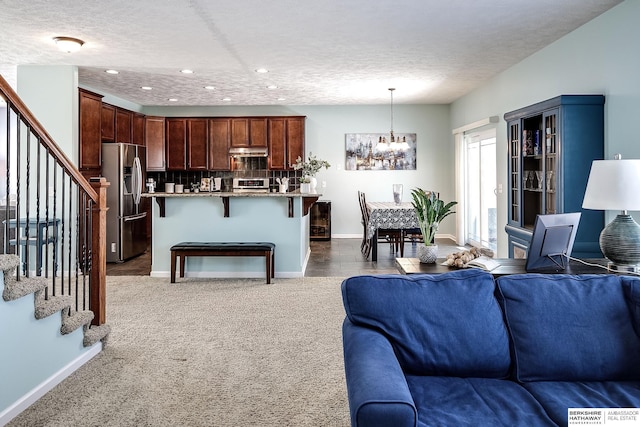 living room featuring a notable chandelier, dark carpet, stairway, a textured ceiling, and baseboards