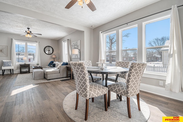 dining space with ceiling fan, a textured ceiling, baseboards, and wood finished floors