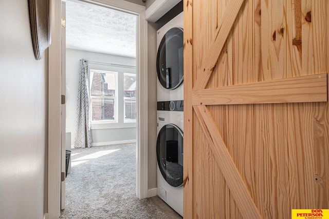 laundry room with a textured ceiling, laundry area, stacked washer / dryer, baseboards, and carpet