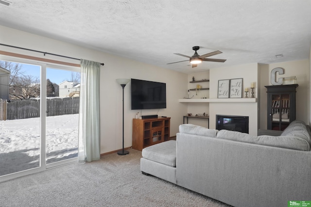 living area featuring a textured ceiling, carpet, a glass covered fireplace, and a ceiling fan