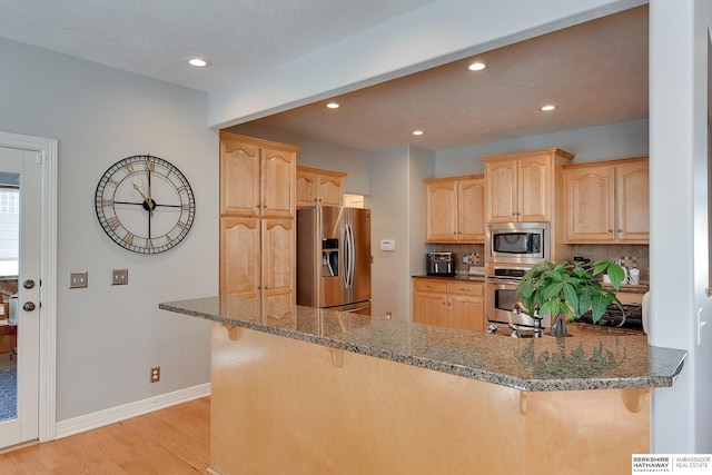 kitchen with dark stone counters, a peninsula, appliances with stainless steel finishes, and a breakfast bar