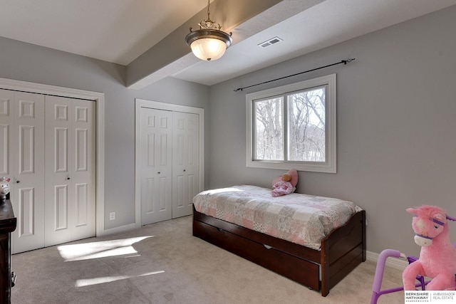 bedroom featuring two closets, light colored carpet, visible vents, beamed ceiling, and baseboards