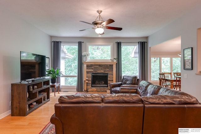 living room with a ceiling fan, a healthy amount of sunlight, a fireplace, and light wood finished floors