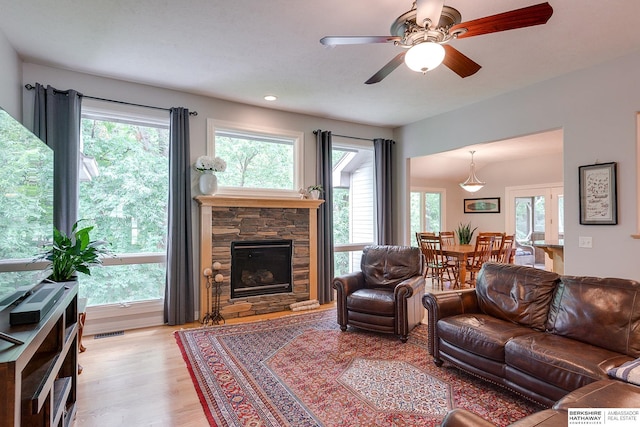 living room featuring a wealth of natural light, a stone fireplace, light wood-style flooring, and visible vents