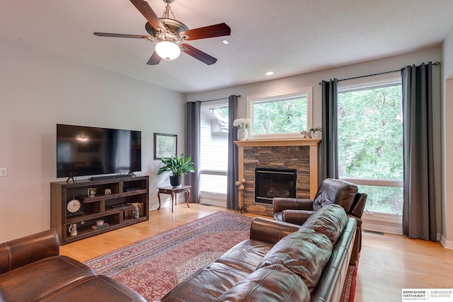 living room featuring light wood-type flooring, a fireplace, visible vents, and a ceiling fan