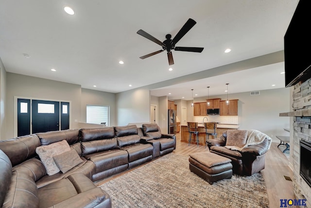 living area featuring a stone fireplace, light wood-type flooring, and recessed lighting