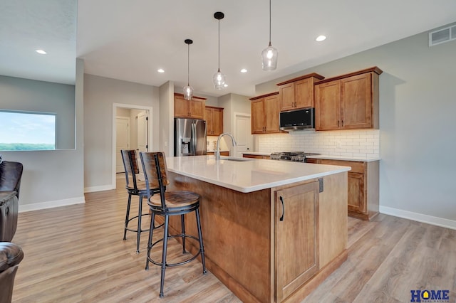 kitchen with light countertops, appliances with stainless steel finishes, a sink, and a kitchen island with sink